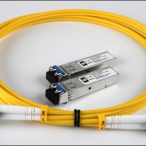 A yellow fiber optic cable with blue connectors and two silver SFP transceivers placed together on a white surface.