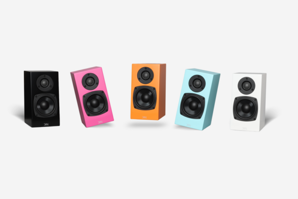 Five **Totem - Kin One - Bookshelf Speakers** in black, pink, orange, blue, and white are arranged side by side on a white background. Each totem-like speaker features two circular drivers.