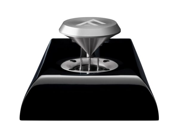 A close-up of a sleek, modern coffee tamper with a metallic finish, positioned on a black base. The tamper features a triangular logo on its top.