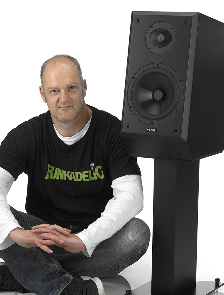 A man sitting on the floor next to a pair of loudspeakers.